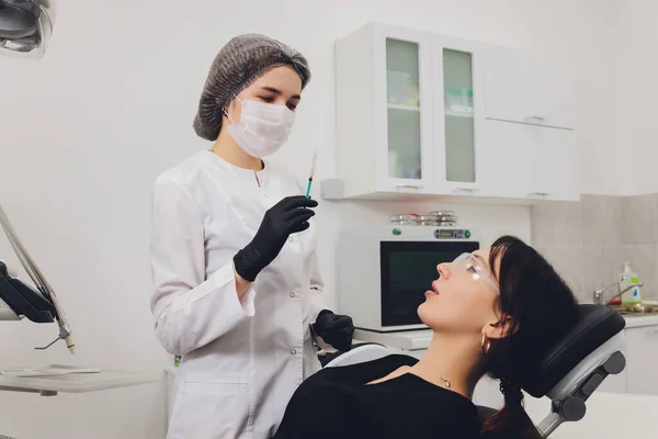 Dentista e paziente che sceglie il trattamento in una consultazione con attrezzature mediche sullo sfondo. — Foto Stock
