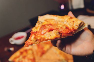 Bir dilim pizzayı elinde tutan bir kadının yakın plan görüntüsü.