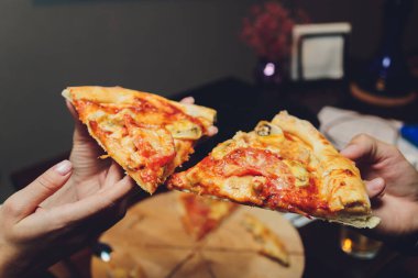 Bir dilim pizzayı elinde tutan bir kadının yakın plan görüntüsü.