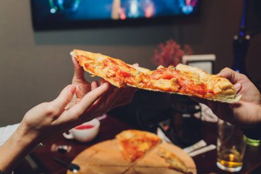 Bir dilim pizzayı elinde tutan bir kadının yakın plan görüntüsü.