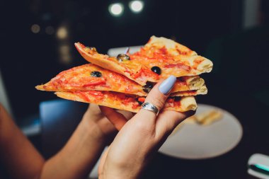 Bir dilim pizzayı elinde tutan bir kadının yakın plan görüntüsü.