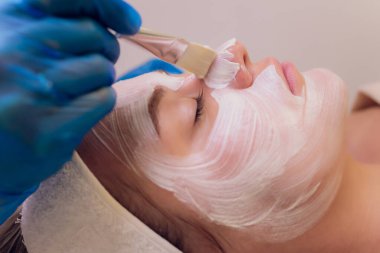 Spa konsepti. Güzellik salonunda besin maskesi takan genç bir kadın, yakın plan. Güzellik uzmanı müşterilerin yüzüne nemlendirici bir maske takar..