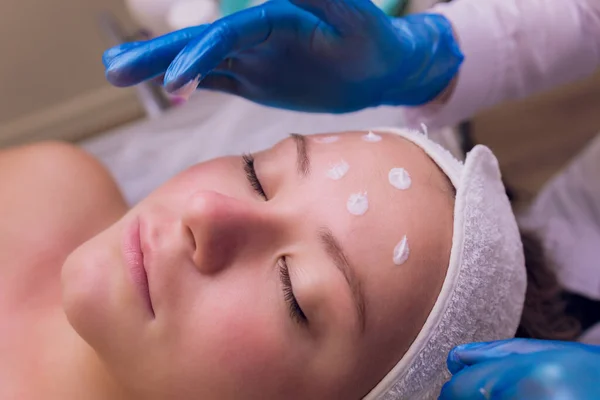 Draufsicht der schönen jungen Frau, die Gesichtshaut behandelt bekommt. Kosmetikerin trägt Creme auf. — Stockfoto