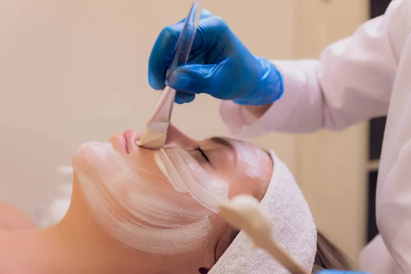 Bovenaanzicht van mooie jonge vrouw krijgen gezichtshuid behandeling. Cosmetici doen de procedure voor het aanbrengen van room. — Stockfoto