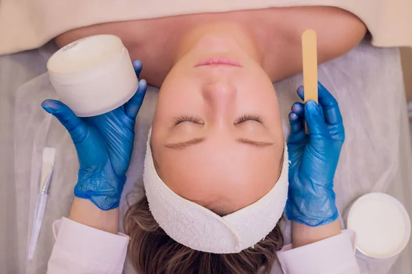 Vista superior de la hermosa mujer joven recibiendo tratamiento de la piel de la cara. Cosmético está llevando a cabo el procedimiento de aplicación de crema. —  Fotos de Stock