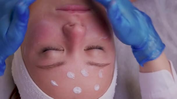 아름다운 젊은 여성이 피부 치료를 받는 장면의 맨 위에 있습니다. 코 스메 티안은 크림을 바르는 과정에 착수하고 있다. — 비디오