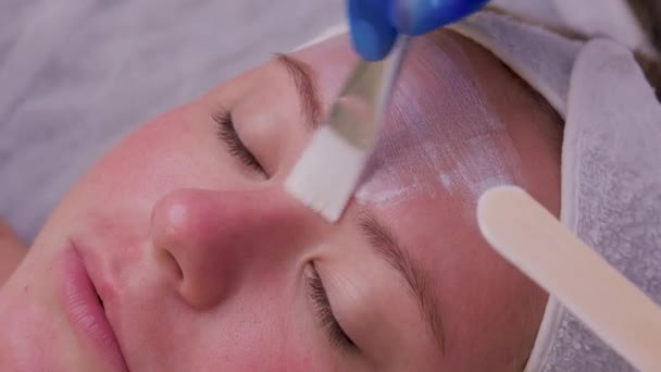 아름다운 젊은 여성이 피부 치료를 받는 장면의 맨 위에 있습니다. 코 스메 티안은 크림을 바르는 과정에 착수하고 있다. — 비디오