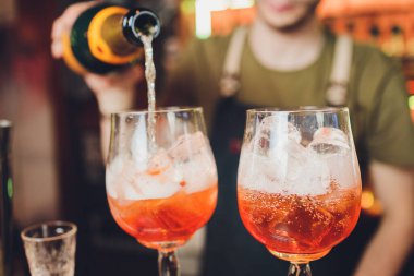 farklı bardaklar, metal zımbırtı ve ölçü kabı tezgahın üzerinde duruyor. Arka planda bulanık barmen.