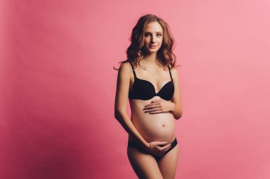 Pembe arka plandaki sırt ağrısını fotokopi alanıyla azaltmak için hamile bir kadının iç çamaşırlı portresi. Ortopedik abdominal destek kemeri kavramı.