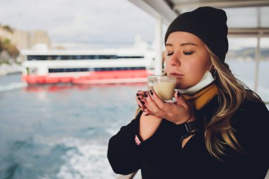 Bir kadın eli, dalgalı su ve uzaktan İstanbul 'daki sisli Bakireler Kulesi' nin arka planında Türk salep sahlep adlı tarçınlı sıcak sütlü bir bardak tutuyor..
