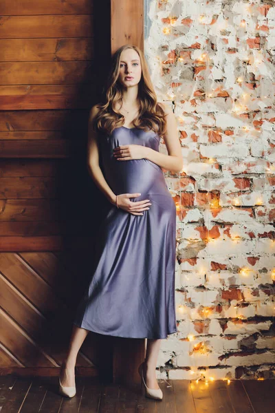 Молода красива вагітна жінка з світлим волоссям і ніжним макіяжем в модному платті позує біля студії . — стокове фото