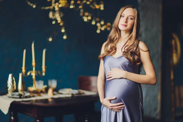 Jovem mulher grávida bonita com cabelo loiro e maquiagem suave em vestido elegante posando perto do estúdio. — Fotografia de Stock