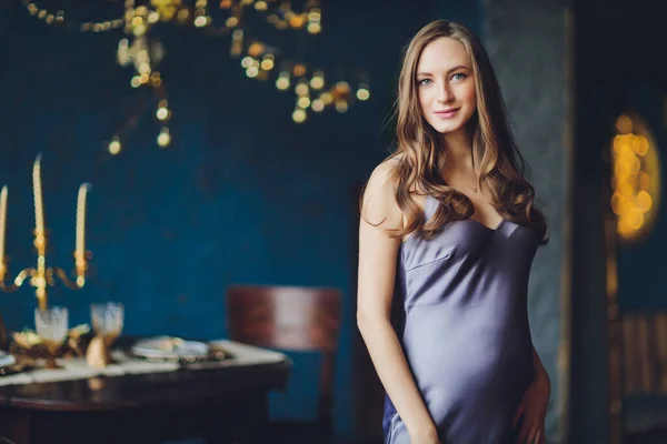 Junge schöne schwangere Frau mit blonden Haaren und sanftem Make-up in modischem Kleid posiert in der Nähe des Studios. — Stockfoto