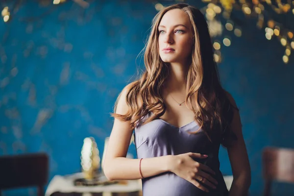Giovane bella donna incinta con i capelli biondi e trucco delicato in abito alla moda posa vicino allo studio. — Foto Stock