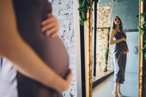 Šťastná těhotná žena se láskyplně dívá na odraz sebe a svého nenarozeného dítěte v zrcadle. — Stock fotografie