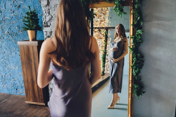 Une femme enceinte heureuse regarde avec amour un reflet d'elle-même et de son bébé à naître dans un miroir. — Photo