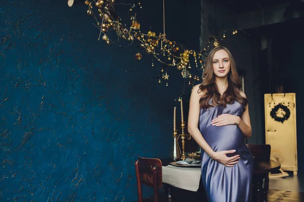 Молодая красивая беременная женщина с светлыми волосами и нежным макияжем в модном платье позирует рядом со студией. — стоковое фото