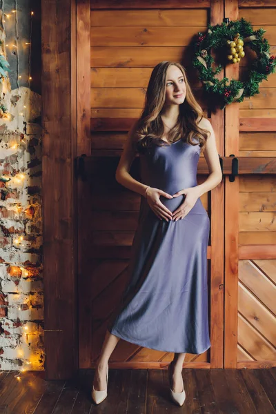 Jovem mulher grávida bonita com cabelo loiro e maquiagem suave em vestido elegante posando perto do estúdio. — Fotografia de Stock
