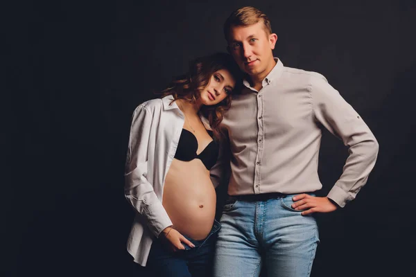 Беременная женщина ее муж держит ее животик. Красивый живот молодой привлекательной беременной женщины на черном фоне. — стоковое фото