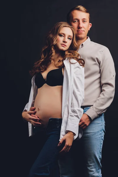 Donna incinta suo marito tenendo la pancia. Bella pancia di giovane donna incinta attraente su sfondo nero. — Foto Stock