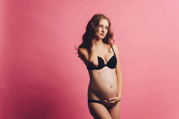 Portrait de bandage de grossesse habillé sur la femme enceinte en sous-vêtements pour réduire les maux de dos au fond rose avec espace de copie. Ceinture de soutien abdominale orthopédique concept. — Photo