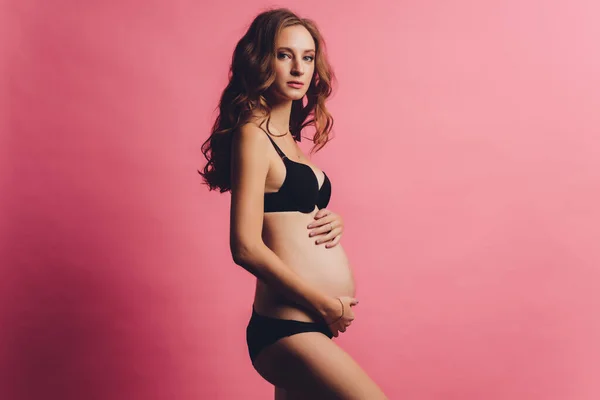 Retrato de bandagem de gravidez vestida em mulher grávida em roupa interior para reduzir a dor nas costas em fundo rosa com espaço de cópia. Conceito de cinto de suporte abdominal ortopédico. — Fotografia de Stock