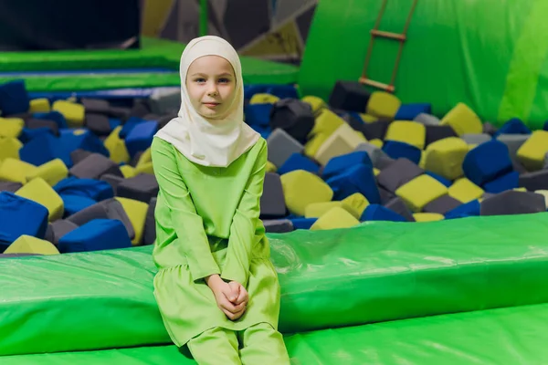 Seitenporträt eines kleinen muslimischen Mädchens, das einen Hijab trägt. Konzept muslimischer Kleidung für Kinder. vor dem Hintergrund des Spielplatzes. — Stockfoto