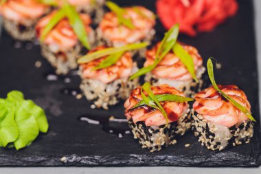 Siyah arka planda somon balıklı Maki Suşi Rolls. Zencefil ve wasabi ile. Suşi menüsü. Japon yemeği. Sushi dürümlü lezzetli Japon yemeklerini yakından çek. Yatay fotoğraf.