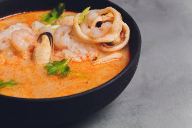 Baharatlı Tayland çorbası Tom Yam, hindistan cevizi sütü, acı biber ve deniz mahsulü karides ve somon ile siyah arka planda. Asya mutfağı, restoran menüsü.