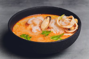 Baharatlı Tayland çorbası Tom Yam, hindistan cevizi sütü, acı biber ve deniz mahsulü karides ve somon ile siyah arka planda. Asya mutfağı, restoran menüsü.