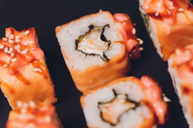 Siyah arka planda somon balıklı Maki Suşi Rolls. Zencefil ve wasabi ile. Suşi menüsü. Japon yemeği. Sushi dürümlü lezzetli Japon yemeklerini yakından çek. Yatay fotoğraf.