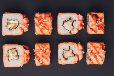Siyah arka planda somon balıklı Maki Suşi Rolls. Zencefil ve wasabi ile. Suşi menüsü. Japon yemeği. Sushi dürümlü lezzetli Japon yemeklerini yakından çek. Yatay fotoğraf.