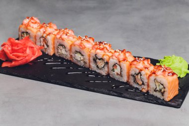 Siyah arka planda somon balıklı Maki Suşi Rolls. Zencefil ve wasabi ile. Suşi menüsü. Japon yemeği. Sushi dürümlü lezzetli Japon yemeklerini yakından çek. Yatay fotoğraf.