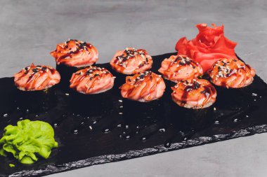 Siyah arka planda somon balıklı Maki Suşi Rolls. Zencefil ve wasabi ile. Suşi menüsü. Japon yemeği. Sushi dürümlü lezzetli Japon yemeklerini yakından çek. Yatay fotoğraf.