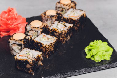 Siyah arka planda somon balıklı Maki Suşi Rolls. Zencefil ve wasabi ile. Suşi menüsü. Japon yemeği. Sushi dürümlü lezzetli Japon yemeklerini yakından çek. Yatay fotoğraf.