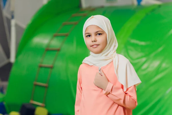 Side portrait of a little Muslim girl wearing a hijab. Concept of Muslim clothing for children. against the background of the playground.