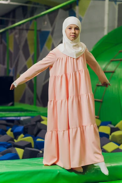 Seitenporträt eines kleinen muslimischen Mädchens, das einen Hijab trägt. Konzept muslimischer Kleidung für Kinder. vor dem Hintergrund des Spielplatzes. — Stockfoto