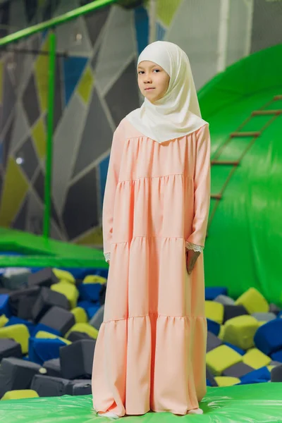 Side portrait of a little Muslim girl wearing a hijab. Concept of Muslim clothing for children. against the background of the playground.