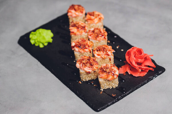 Маки Суши Роллс с лосося на черном камне на темном фоне. С имбирем и васаби. Меню суши. Японская еда. Крупный план вкусной японской еды с суши-роллом. Горизонтальное фото.