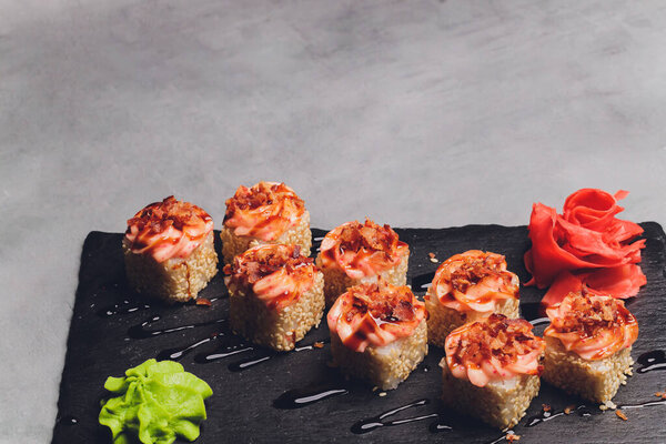 Маки Суши Роллс с лосося на черном камне на темном фоне. С имбирем и васаби. Меню суши. Японская еда. Крупный план вкусной японской еды с суши-роллом. Горизонтальное фото.