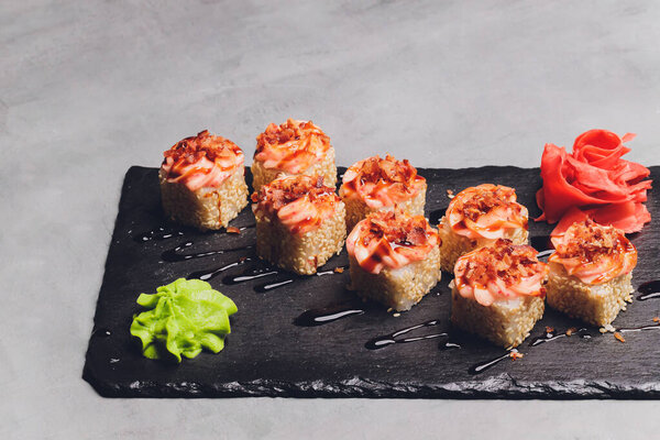 Маки Суши Роллс с лосося на черном камне на темном фоне. С имбирем и васаби. Меню суши. Японская еда. Крупный план вкусной японской еды с суши-роллом. Горизонтальное фото.