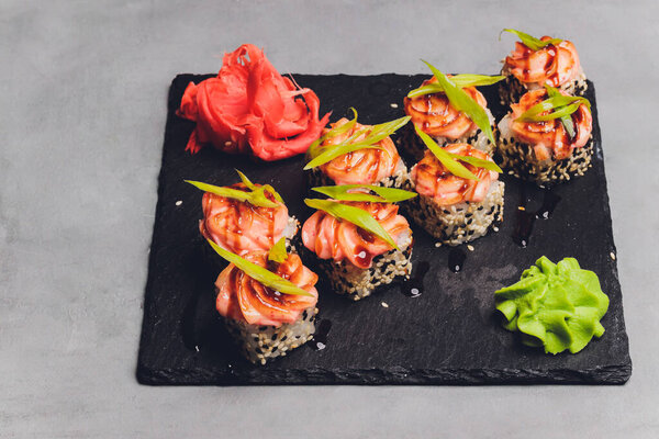 Маки Суши Роллс с лосося на черном камне на темном фоне. С имбирем и васаби. Меню суши. Японская еда. Крупный план вкусной японской еды с суши-роллом. Горизонтальное фото.