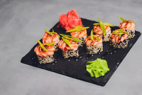 Rollos de sushi Maki con salmón sobre piedra negra sobre fondo oscuro. Con jengibre y wasabi. Menú de sushi. Comida japonesa. Primer plano de deliciosa comida japonesa con rollo de sushi. Fotografía horizontal. — Foto de Stock