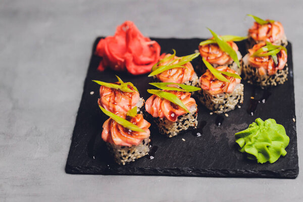 Маки Суши Роллс с лосося на черном камне на темном фоне. С имбирем и васаби. Меню суши. Японская еда. Крупный план вкусной японской еды с суши-роллом. Горизонтальное фото.