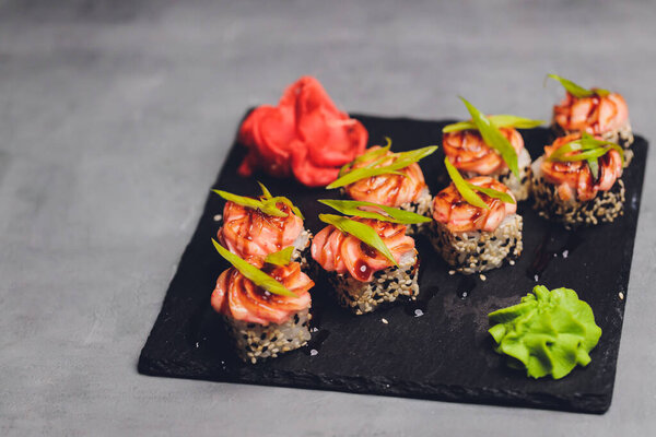 Маки Суши Роллс с лосося на черном камне на темном фоне. С имбирем и васаби. Меню суши. Японская еда. Крупный план вкусной японской еды с суши-роллом. Горизонтальное фото.