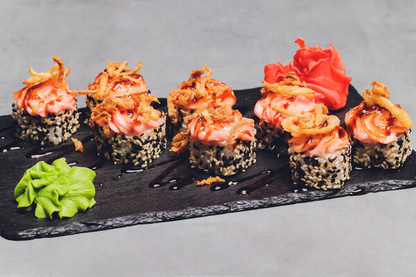 Маки Суши Роллс с лосося на черном камне на темном фоне. С имбирем и васаби. Меню суши. Японская еда. Крупный план вкусной японской еды с суши-роллом. Горизонтальное фото.