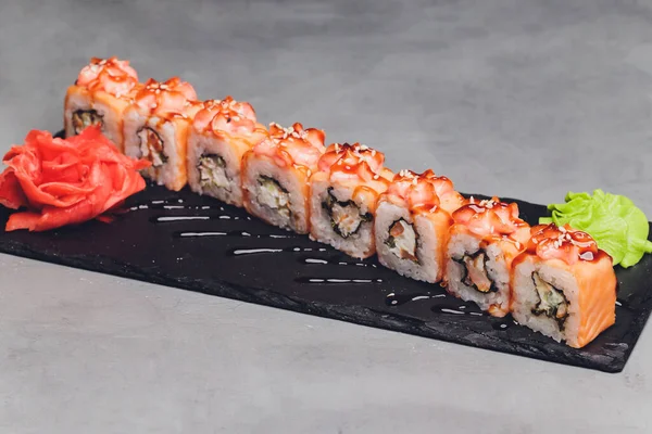 Маки Суши Роллс с лосося на черном камне на темном фоне. С имбирем и васаби. Меню суши. Японская еда. Крупный план вкусной японской еды с суши-роллом. Горизонтальное фото. — стоковое фото