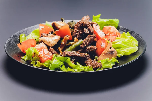 Salade de tagliata de bœuf tranchée avec haricots verts, tomates cerises, roquette fraîche et quartiers de parmesan et de citron vert, servie sur une assiette noire. — Photo
