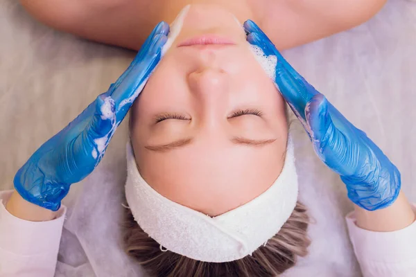 Vista superior de la hermosa mujer joven recibiendo tratamiento de la piel de la cara. Cosmético está llevando a cabo el procedimiento de aplicación de crema. —  Fotos de Stock