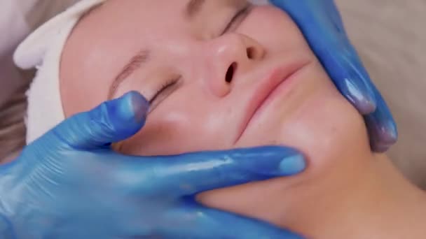 Top view of beautiful young woman getting face skin treatment. Cosmetician is undertaking the procedure applying cream. — Stock Video